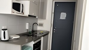 A compact kitchen with white cabinets, a black countertop, a sink, a dishwasher, and a microwave. - Hermoso estudio en Santiago (Santiago)