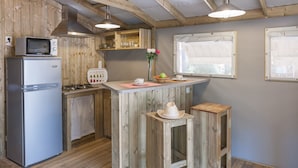 A compact kitchen with wooden walls and a central island, equipped with a refrigerator, microwave, and stove. - Huttopia Parque de Doñana  (Hinojos)