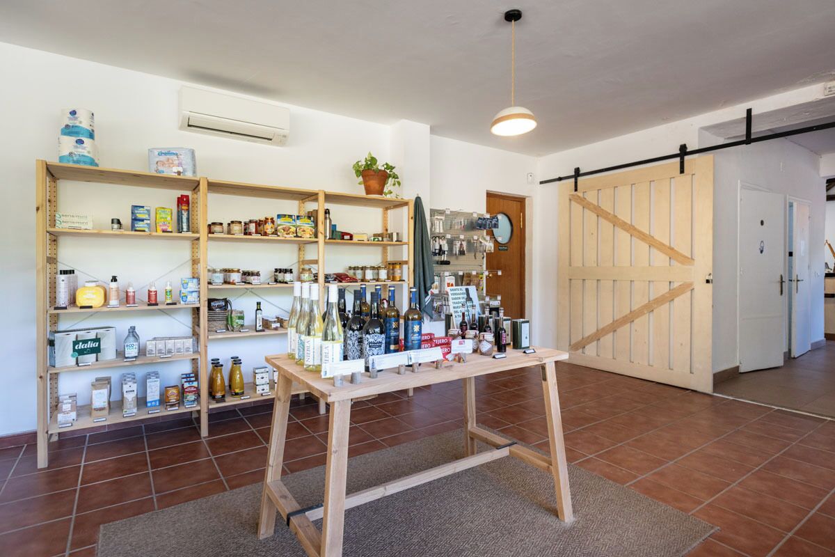 Una habitación con estanterías de madera llenas de alimentos y bebidas, una mesa de madera con botellas y una puerta corredera al fondo.