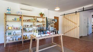 Una habitación con estanterías de madera llenas de alimentos y bebidas, una mesa de madera con botellas y una puerta corredera al fondo.