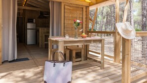 A wooden deck with a table, a vase with flowers, a hat, and a refrigerator in the background. - Huttopia Parque de Doñana  (Hinojos)