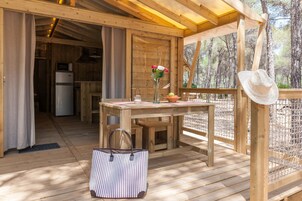 Una terraza de madera con una mesa, un jarrón con flores, un sombrero y un refrigerador al fondo.