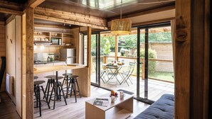 A modern kitchen with wooden beams, a dining area with a table and chairs, and a large sliding glass door leading to a deck. - Huttopia Parque de Doñana  (Hinojos)