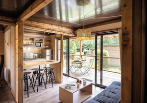 Una cocina moderna con vigas de madera, un comedor con mesa y sillas, y un gran ventanal corredizo que da a una terraza.