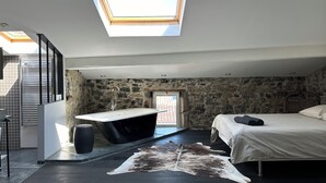 Un dormitorio moderno con tragaluz, pared de piedra, cama grande y baño con bañera.