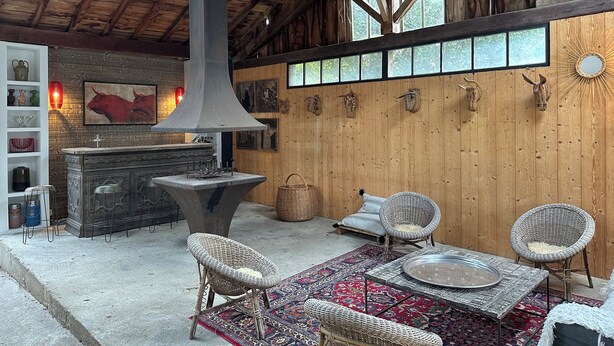 Un interior rústico de madera con una chimenea grande, muebles de mimbre y una alfombra estampada.