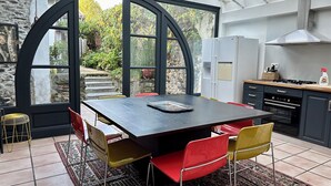 Una cocina moderna con una isla grande, un comedor con sillas y vistas al jardín a través de amplios ventanales.