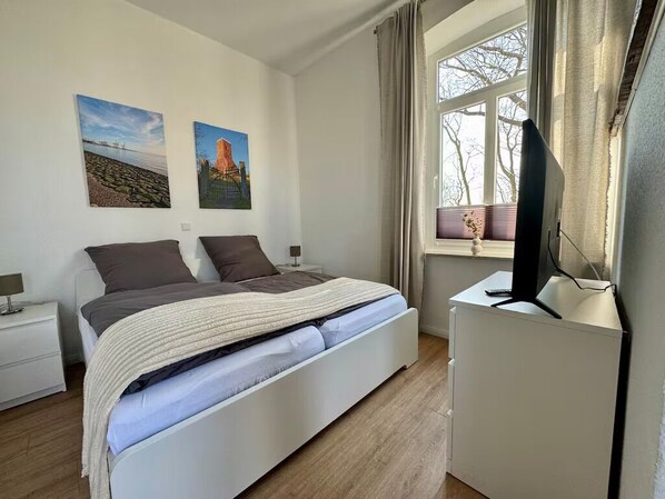 Un dormitorio con cama, escritorio y ventana con cortinas.