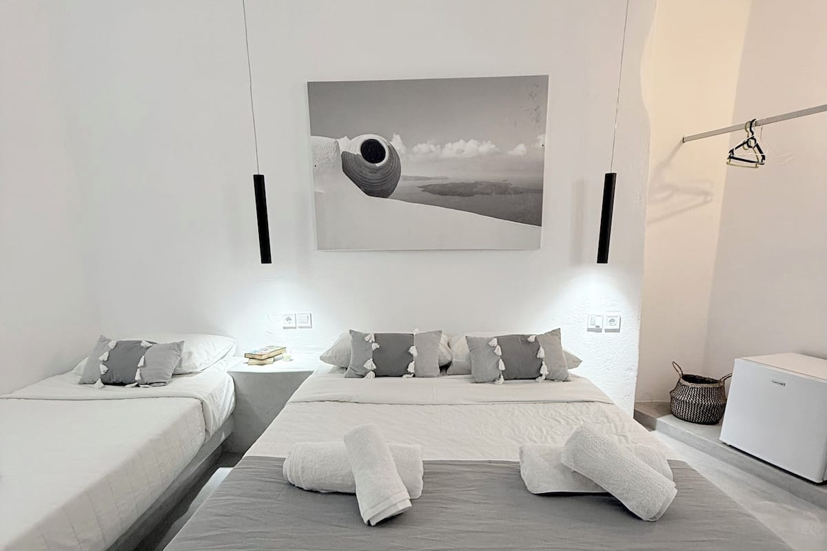 A modern bedroom with two beds, a large painting, and a white wardrobe.