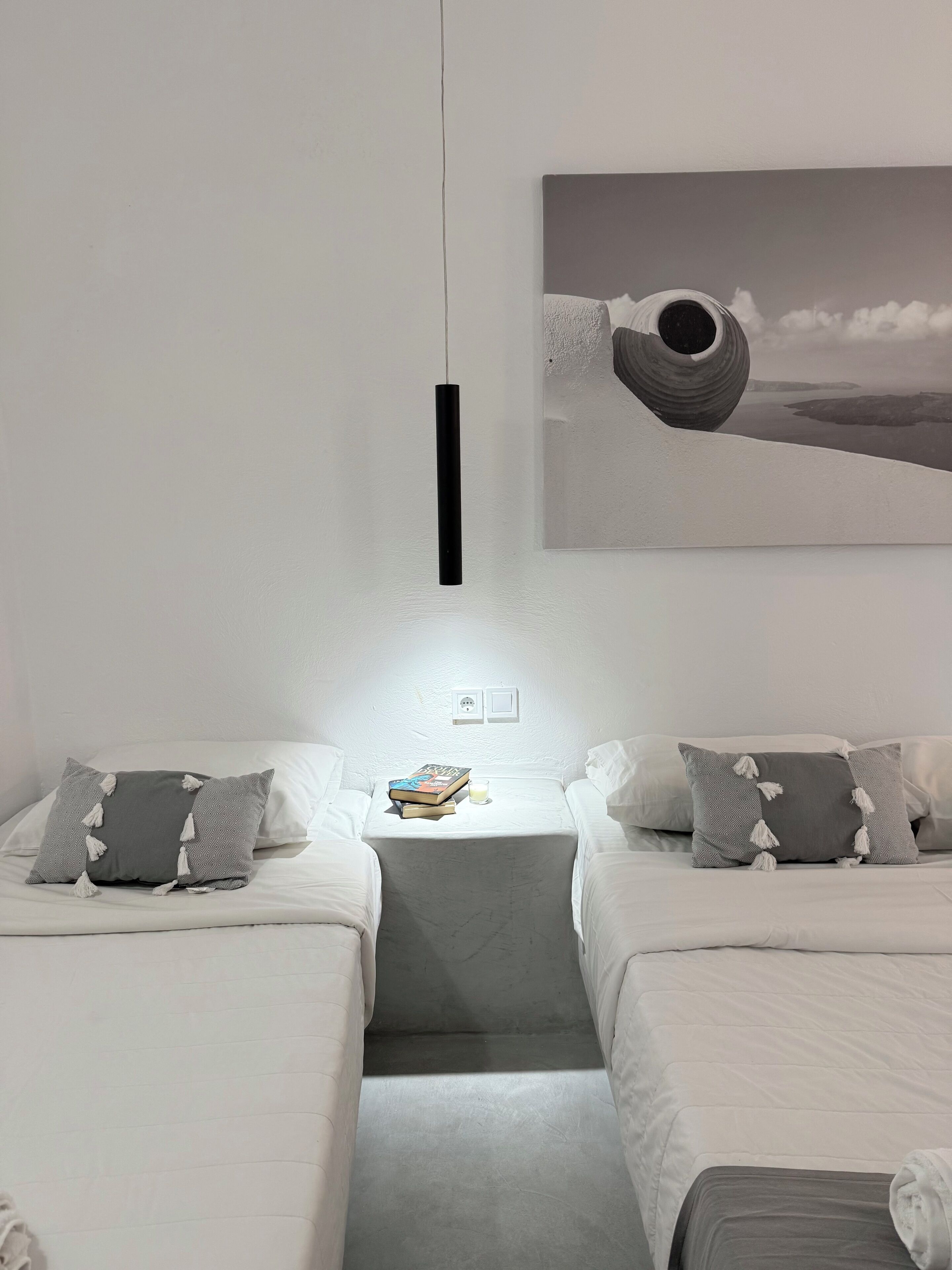 A hotel room with two beds, a small table with books and a glass, and a painting on the wall.