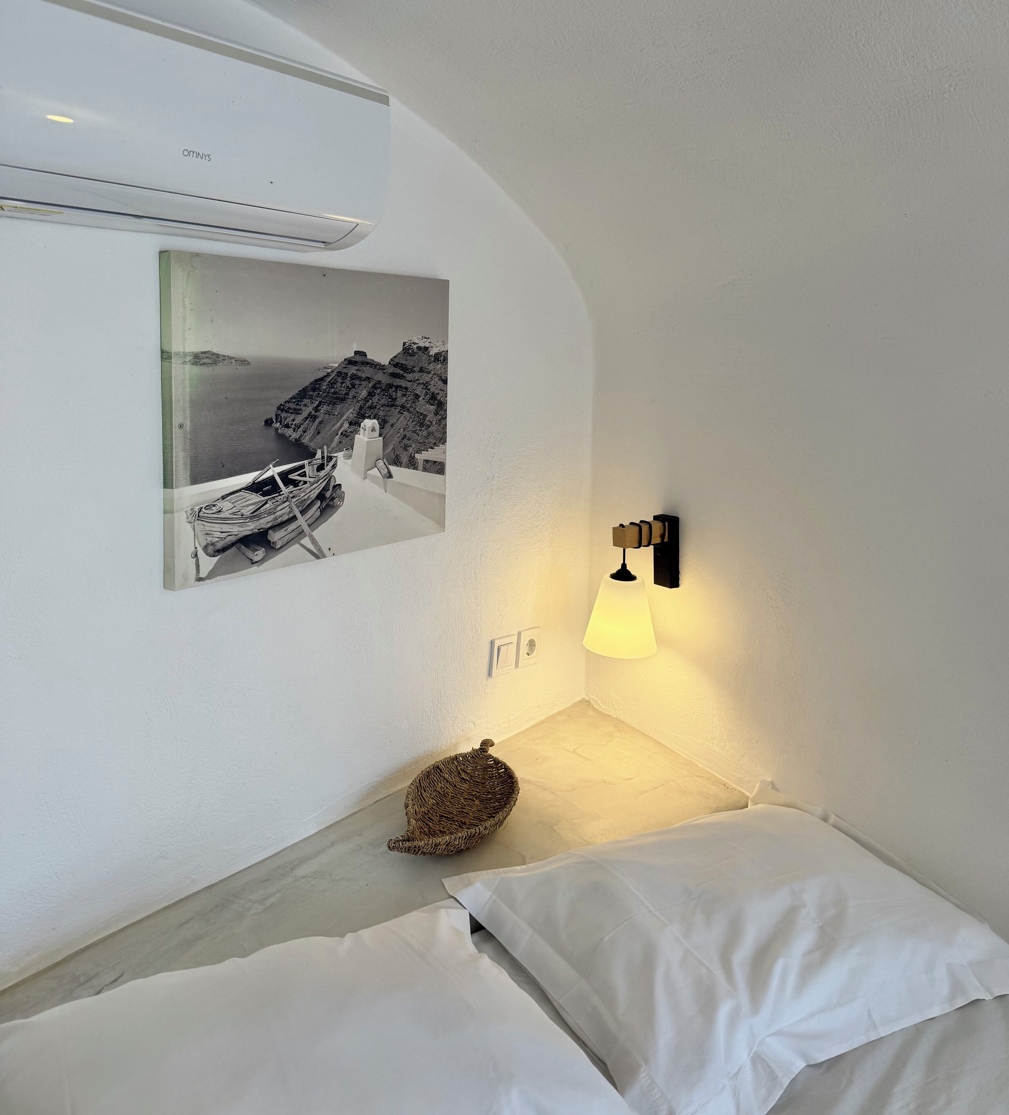A hotel room with a bed, a wall-mounted air conditioner, a wall-mounted lamp, and a framed picture of a boat on the wall.