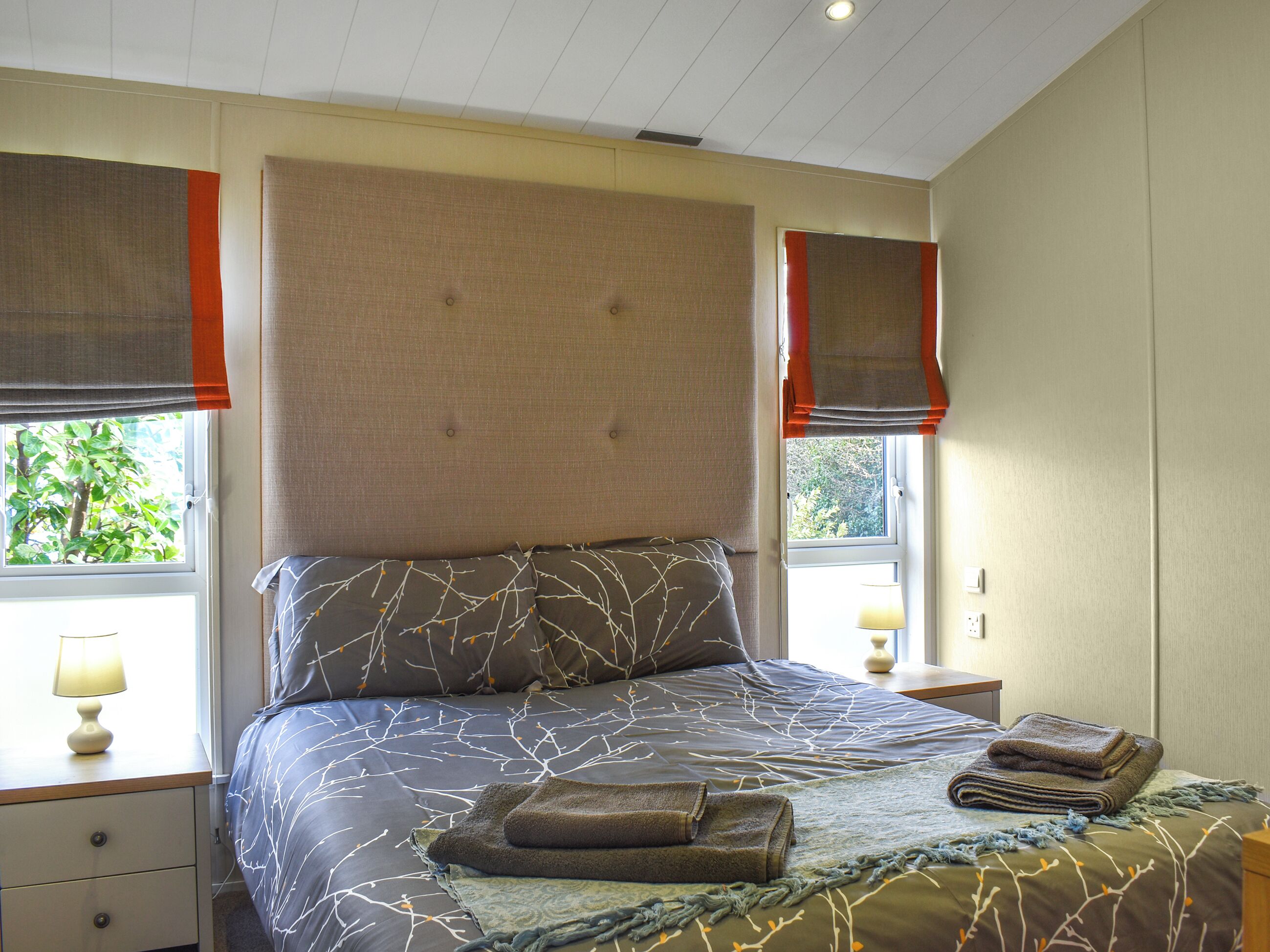 A bedroom with a large bed, two bedside tables, a nightstand, and a window with a view of greenery.