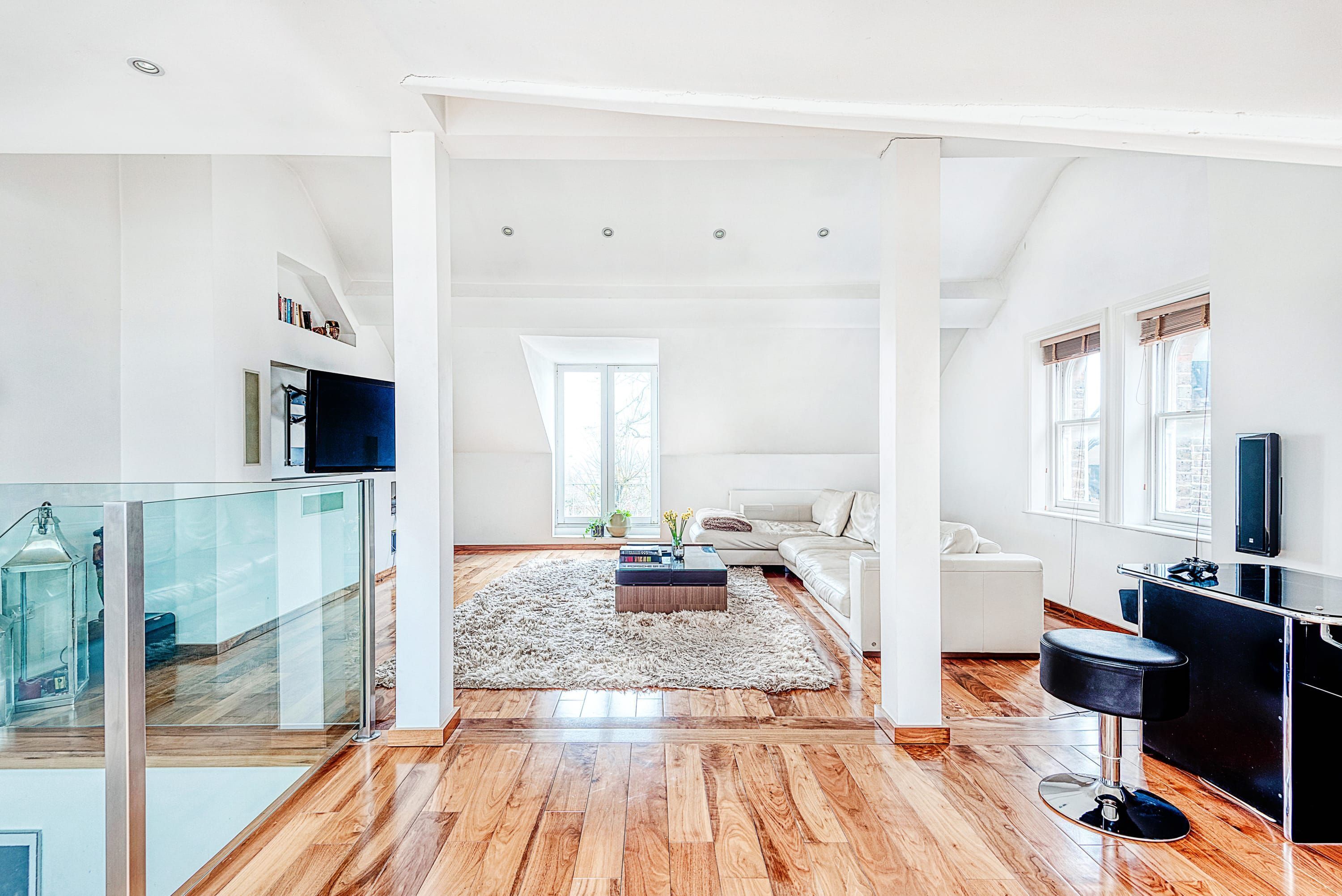 A spacious living area with a wooden floor, a large rug, a sofa, a coffee table, and a TV.
