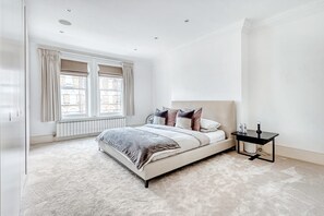 Un dormitorio con una cama grande, una mesita de noche y un ventanal con cortinas.