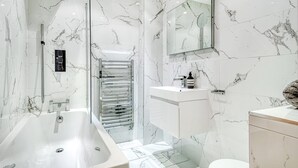 A modern bathroom with a large bathtub, a glass shower enclosure, and a marble-tiled wall. - The King of Spades - by Out of Office Lifestyle (London)