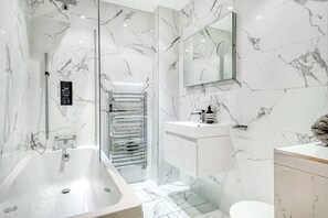 A modern bathroom with a large bathtub, a glass shower enclosure, and a marble-tiled wall. - The King of Spades - by Out of Office Lifestyle (London)
