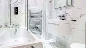 A modern bathroom with a marble wall, a large bathtub, a glass shower enclosure, and a white sink with a mirror above it. - The King of Spades - by Out of Office Lifestyle (London)