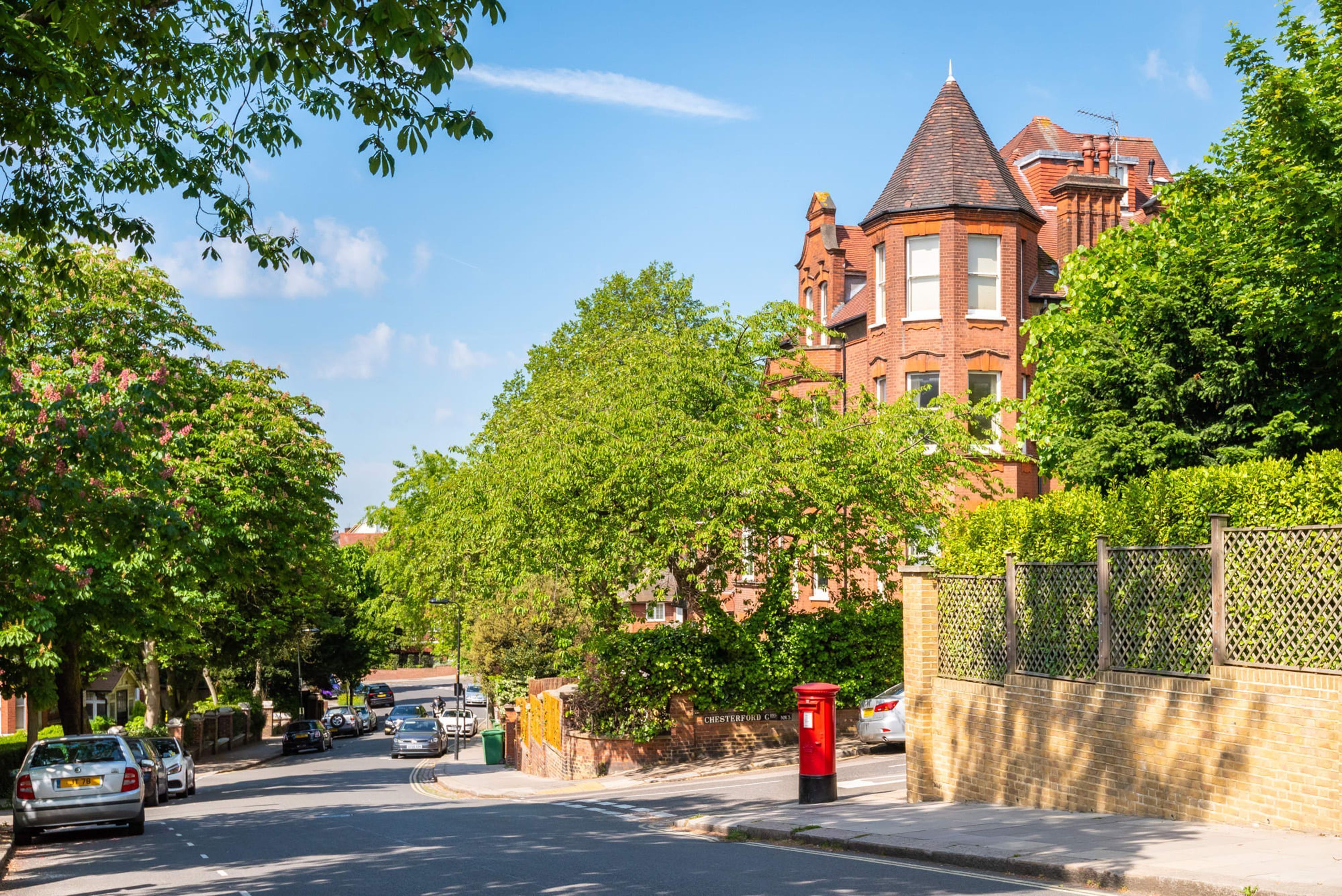A street with parked cars, a red post box, and a large brick building with a tower.