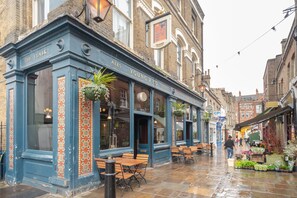 Un pub tradicional con terraza, un cartel que dice "Ales Young & Co Stout" y una entrada visible.
