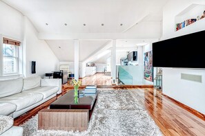 A spacious living area with a white sofa, a coffee table with books, a fluffy rug, and a large TV on the wall. - The King of Spades - by Out of Office Lifestyle (London)