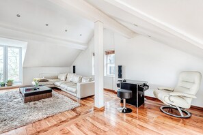 A modern loft bedroom with a sloped ceiling, a white sofa, a white armchair, a small black table, and a fluffy rug.