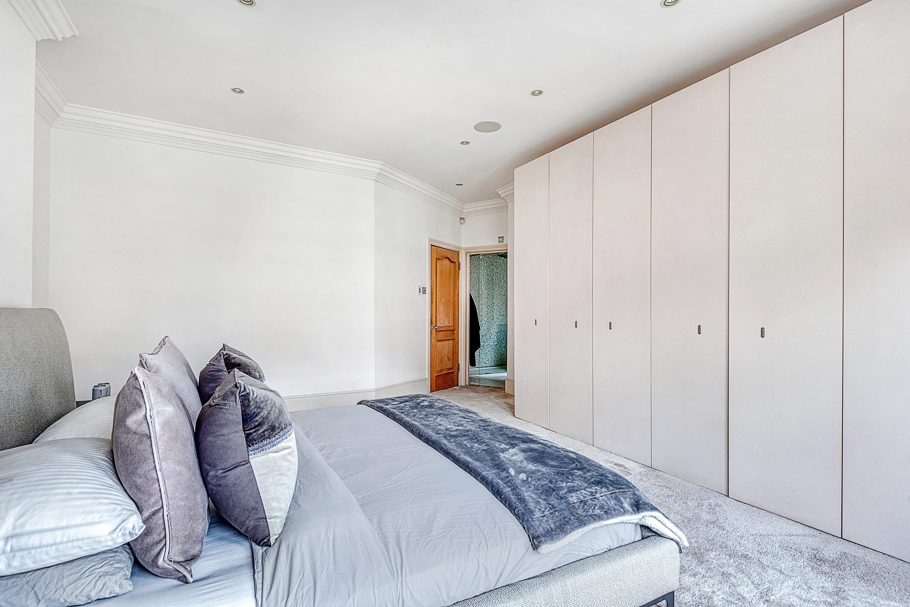 A bedroom with a bed, pillows, a grey sofa, and a wardrobe.