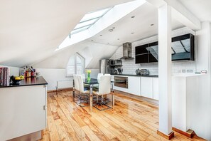 A modern kitchen with white cabinetry, a dining area with a table and chairs, and a skylight above. - The King of Spades - by Out of Office Lifestyle (London)