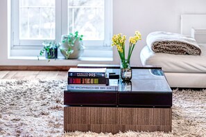 A living room with a coffee table holding books and a vase with flowers. - The King of Spades - by Out of Office Lifestyle (London)