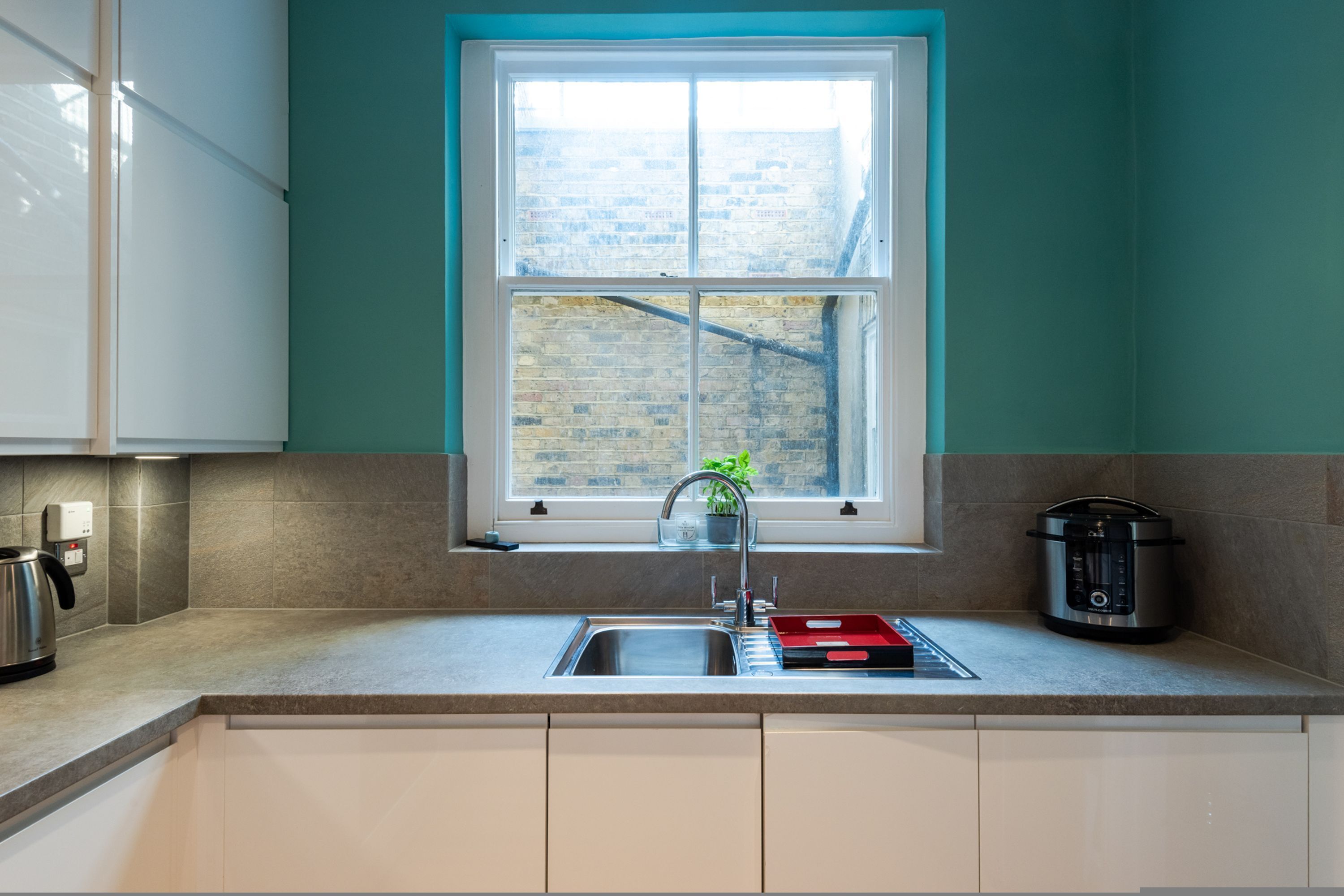 A modern kitchen with a window, a sink, a kettle, and a slow cooker.