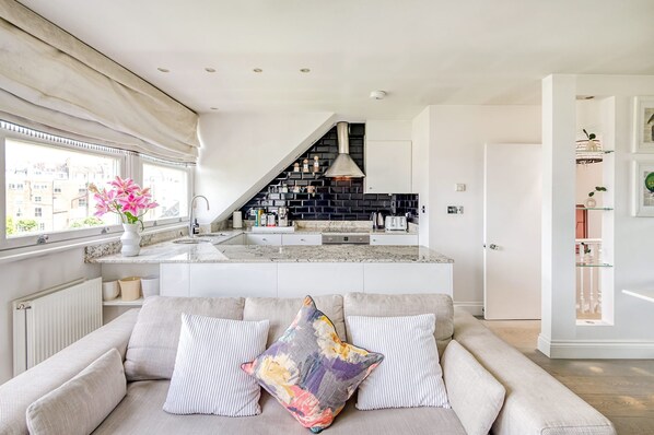 A modern kitchen with a black backsplash, white cabinetry, and a built-in island. - The Luxury Treehouse - One bed Little Venice - by Out of Office Lifestyle (London)