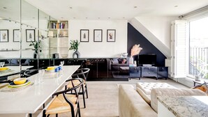 A modern kitchen with a dining area, a living room with a sofa and TV, and a large window with a view. - The Luxury Treehouse - One bed Little Venice - by Out of Office Lifestyle (London)