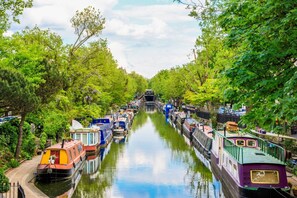 A narrow canal lined with colorful boats and lush green trees. - The Luxury Treehouse - One bed Little Venice - by Out of Office Lifestyle (London)