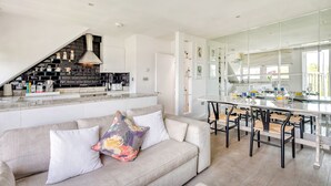 A modern kitchen with a built-in stove, a dining area with bar stools, and a large mirror. - The Luxury Treehouse - One bed Little Venice - by Out of Office Lifestyle (London)
