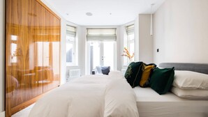 A bedroom with a large bed, a wooden wardrobe, and a window with a view. - The English Gentleman Hampstead Heath - by Out of Office Lifestyle (London)
