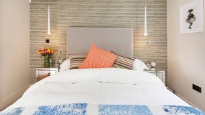 A modern bedroom with a large bed, striped pillows, a vase of flowers, and a framed artwork on the wall. - The Bohemian Rhapsody- Garden Apartment in Hampstead - by Out of Office Lifestyle (London)