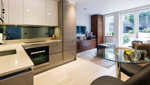 A modern kitchen with stainless steel appliances, a glass dining table, and a view of the garden through large windows. - The Bohemian Rhapsody- Garden Apartment in Hampstead - by Out of Office Lifestyle (London)