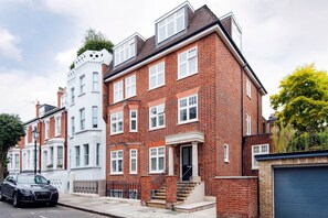 A row of terraced houses with a mix of brick and white facades, a car parked on the street, and a tree to the right. - The Bohemian Rhapsody- Garden Apartment in Hampstead - by Out of Office Lifestyle (London)
