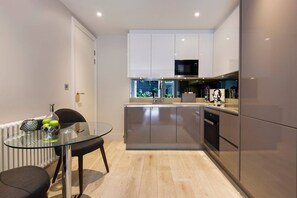 A modern kitchen with a glass dining table, stainless steel appliances, and white cabinetry. - The Bohemian Rhapsody- Garden Apartment in Hampstead - by Out of Office Lifestyle (London)