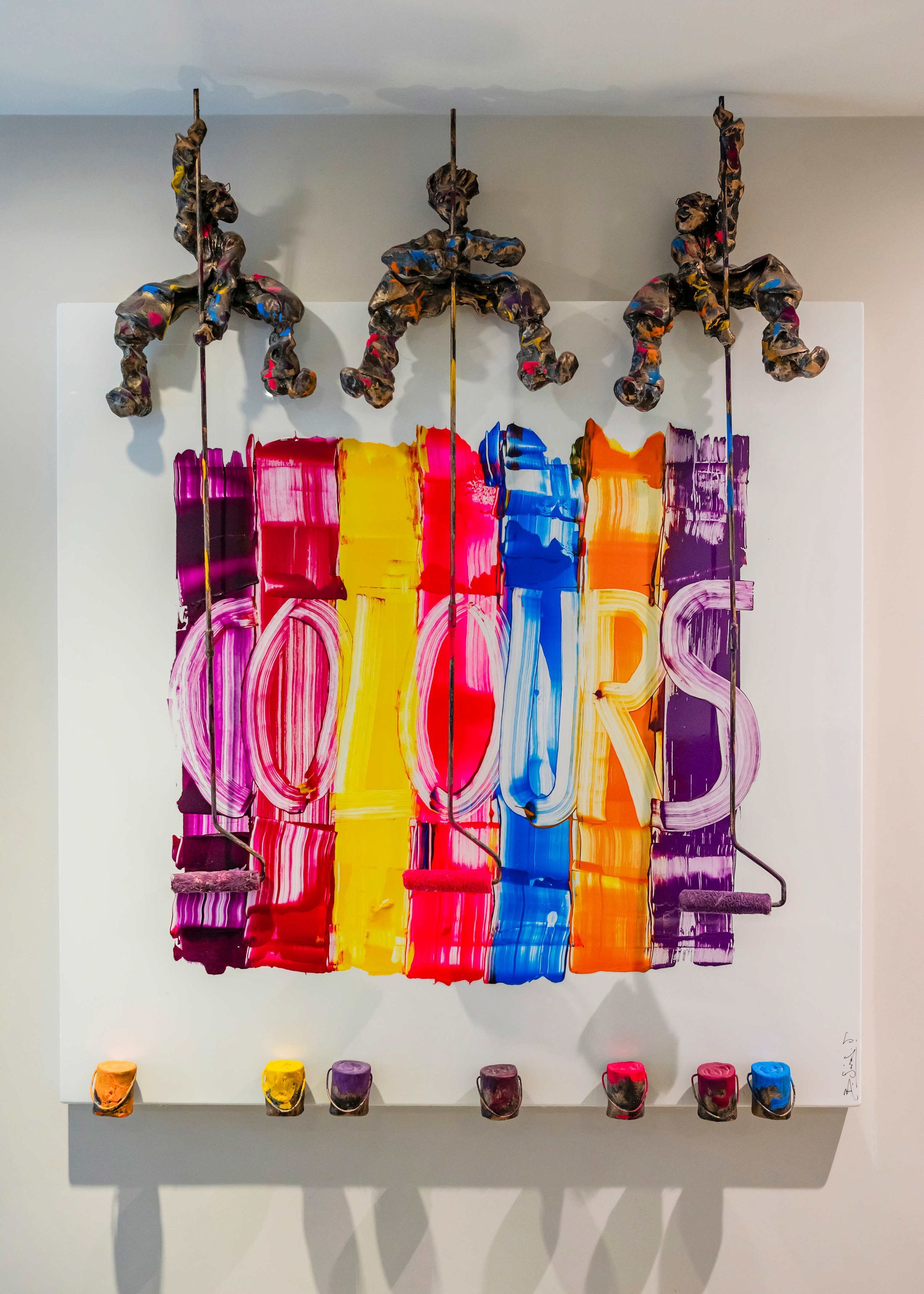 A wall with a colorful abstract painting and a row of paint cans below.
