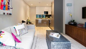 A modern living room with a sofa, coffee table, and a kitchen in the background. - The Bohemian Rhapsody- Garden Apartment in Hampstead - by Out of Office Lifestyle (London)