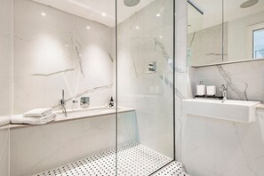 A modern bathroom with a glass-enclosed shower, a marble-tiled wall, a white sink, and a large mirror.