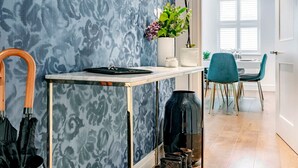 A modern room with a patterned blue wall, a round mirror, a vase with flowers, a table with a tray, and a pair of boots. - The Smooth Velvet - by Out of Office Lifestyle (London)