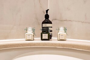 A bathroom counter with three scented candles labeled HOPE, LOVE, and HOPE, and a bottle of hand wash soap.