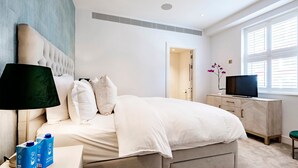 A modern bedroom with a large bed, bedside tables, a TV, and a window with blinds. - The Smooth Velvet - by Out of Office Lifestyle (London)
