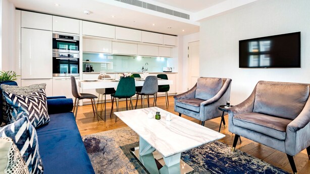 A modern living room with a sofa, two armchairs, a coffee table, and a dining area with chairs and a kitchen in the background. - The Smooth Velvet - by Out of Office Lifestyle (London)