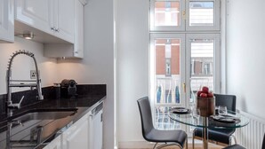 A compact kitchen with a black countertop, white cabinets, and a window with a view of buildings. - The Mayfair Muse - by Out of Office Lifestyle (London)