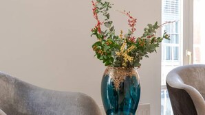 A modern living room with a grey velvet armchair, a blue vase with flowers, and a gold-framed mirror on a small table. - The Mayfair Muse - by Out of Office Lifestyle (London)