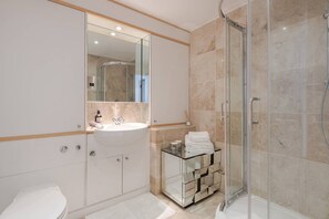 Een moderne badkamer met een douchecabine van glas, een wit wastafelmeubel en een glazen blad.