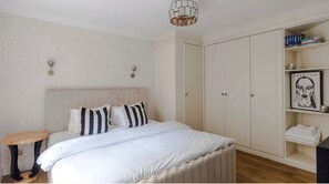 A bedroom with a bed, bedside tables, a wardrobe, and a shelf with books. - The Mayfair Muse - by Out of Office Lifestyle (London)