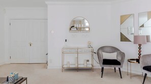 A modern, minimalist room with a white door, a console table with glassware, a grey armchair, and a lamp. - The Mayfair Muse - by Out of Office Lifestyle (London)
